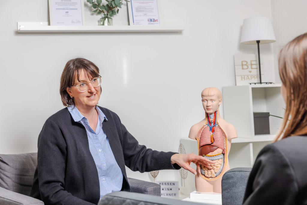 Andrea Schober erklärt in Beratungssituation an medizinischer Organuhr – Ernährungstherapie und Beratung bei Essen in Balance